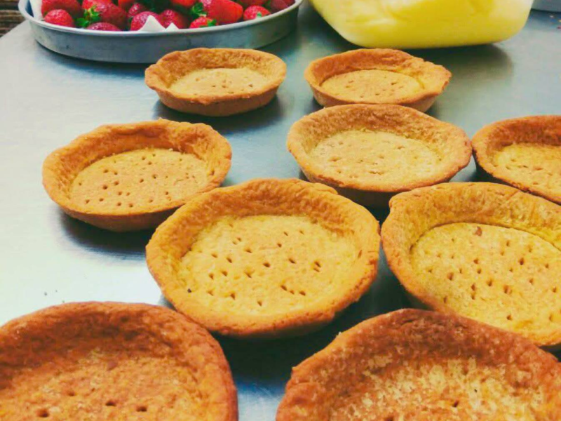 Freshly baked tart shells and strawberries on a stainless steel counter