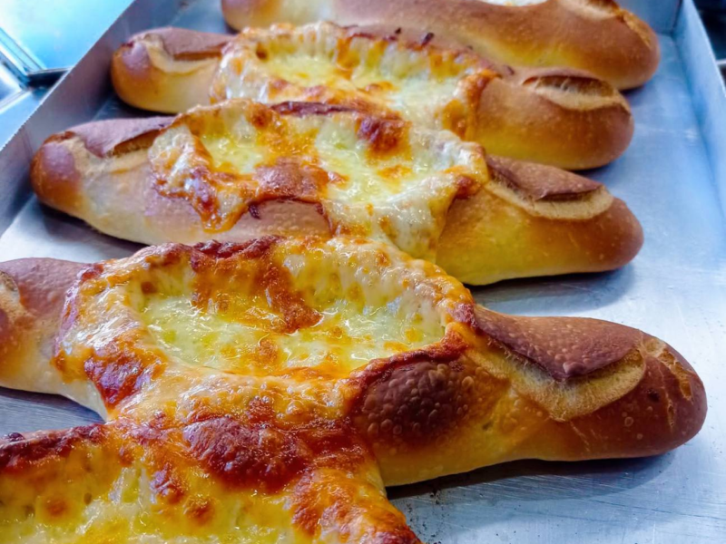 Close-up of freshly baked, cheese-topped bread loaves on a metal tray