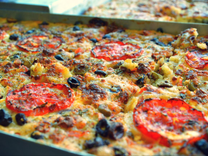 Close-up of a freshly baked, cheesy pizza topped with sliced tomatoes and black olives