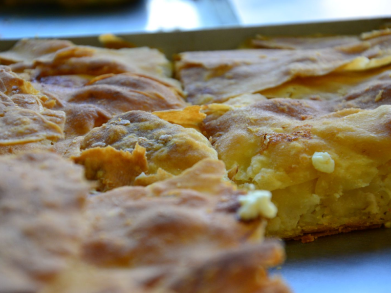 Close-up of golden-brown, flaky phyllo dough pie with a savory filling, possibly cheese or spinach.