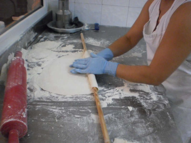 Person in blue gloves rolling out dough with a wooden rolling pin