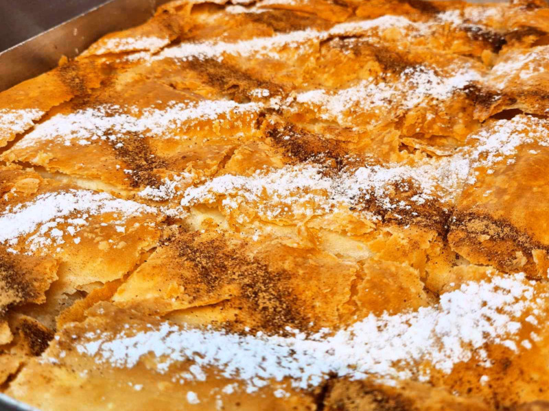 Close-up of a golden-brown baked phyllo pastry dish dusted with powdered sugar and cinnamon