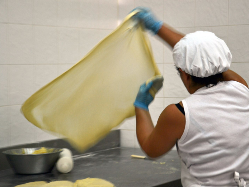 Baker in gloves stretching thin dough over a counter